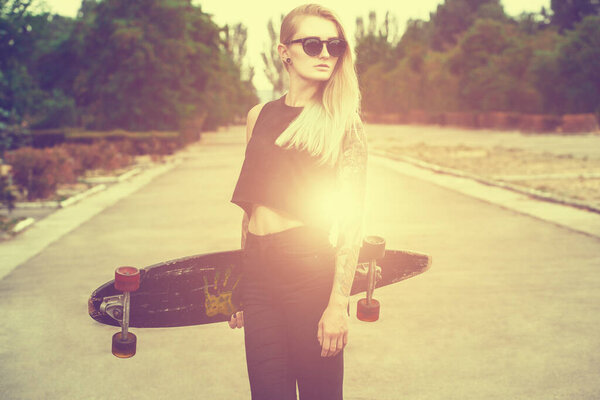 Красивая, сексуальная блондинка-хипстер с голубыми волосами в татуировке стоит с длинной доской на улице
.