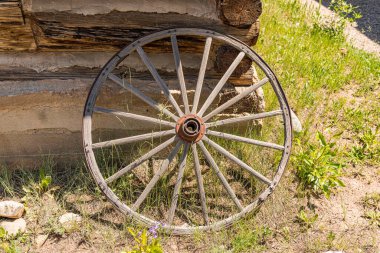 Yaşlı yıpranmış araba tekerleği kütük bir kulübe duvarına yaslanıyor.