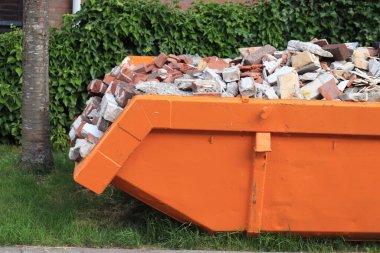 Old, demolished bricks in an orange garbage dumpster