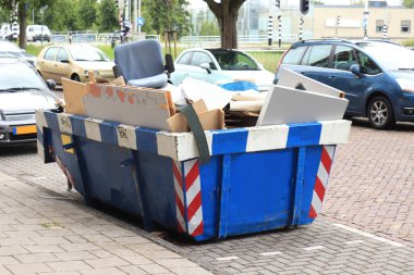 Mavi çöp konteynırı ve eski ofis ekipmanlarıyla dolu.