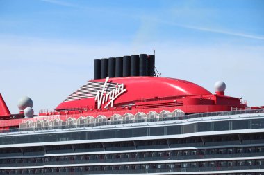 IJmuiden, The Netherlands - April 20th, 2022:  Valiant Lady cruise ship, operated by Virgin Voyages, shipbuilder Fincantieri. Detail of the red funnel with Virgin company logo