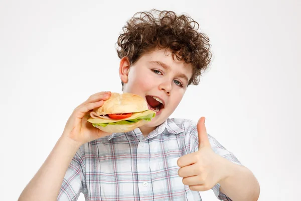 Menino comendo sanduíche grande mostrando sinal OK — Fotografia de Stock