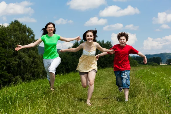 Famille active - mère et enfants courant, sautant en plein air — Photo