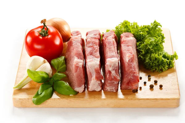 Rauw varkensvlees op snijplank en groenten — Stockfoto