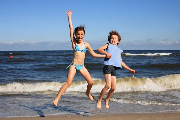 Tonårig flicka och pojke hoppning, kör på stranden — Stockfoto