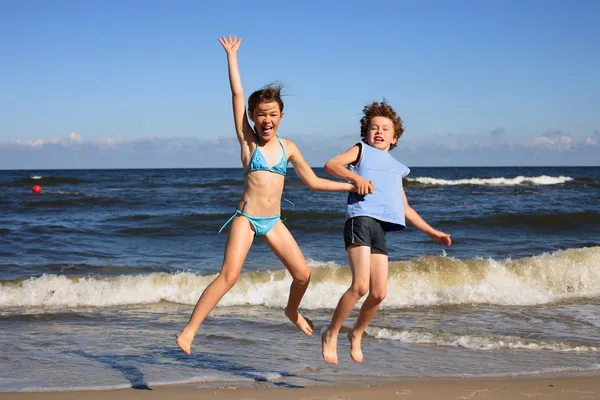 Teenage girl and boy jumping, running on beach — Stock Photo, Image