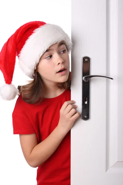 Menina com chapéu de Papai Noel espreitando atrás da porta — Fotografia de Stock