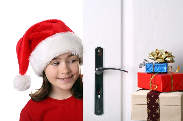 Menina com chapéu de Papai Noel espreitando atrás da porta — Fotografia de Stock