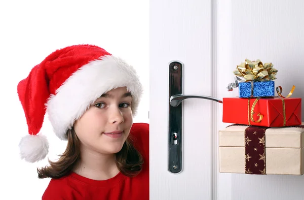 Menina com chapéu de Papai Noel espreitando atrás da porta — Fotografia de Stock