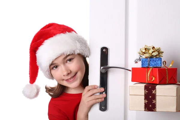 Menina com chapéu de Papai Noel espreitando atrás da porta — Fotografia de Stock
