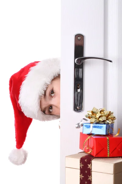 Menina com chapéu de Papai Noel espreitando atrás da porta — Fotografia de Stock