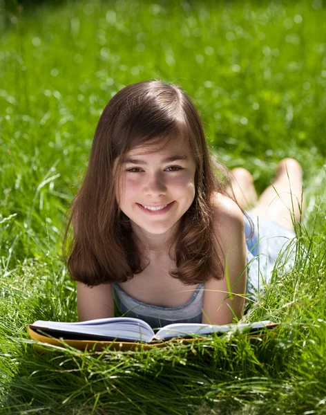 Дівчина лежить на зеленому лузі читає книгу — стокове фото