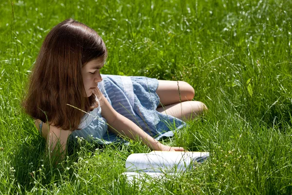 Meisje liggen op groene weide lezen van boek — Stockfoto