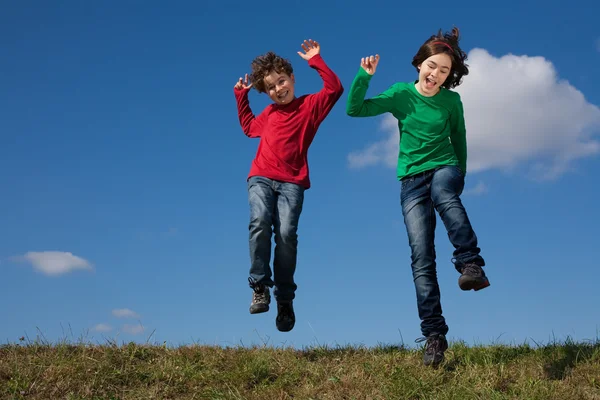 Niños saltando contra el cielo azul — Foto de Stock