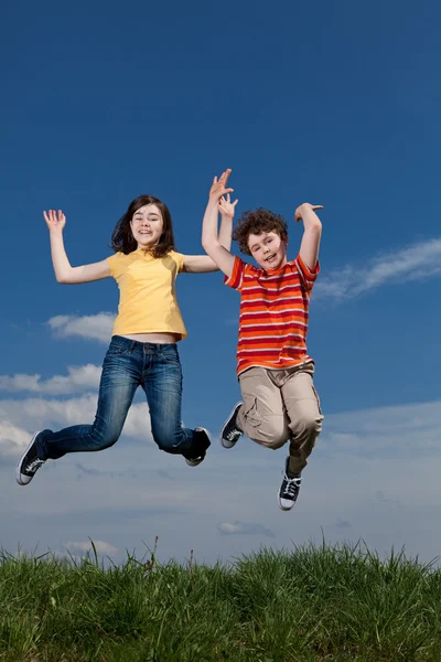 Menina e menino pulando contra o céu azul — Fotografia de Stock