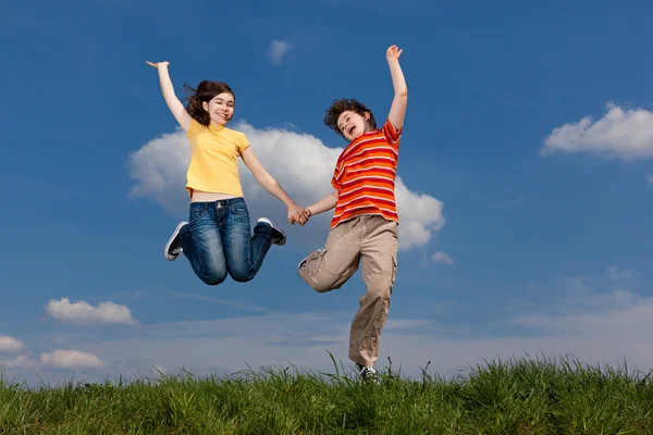 Menina e menino pulando contra o céu azul — Fotografia de Stock