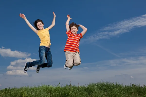 Girl and boy jumping against blue sky — Stock Photo, Image