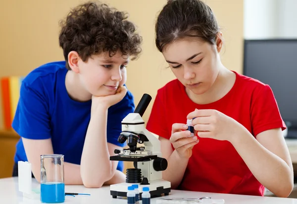 Niña y niño examinando la preparación bajo el microscopio — Foto de Stock