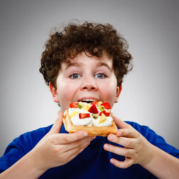 Menino comer bolo com creme e frutas — Fotografia de Stock