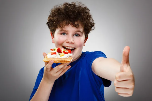 Boy eating cake with cream and fruits — Stock Photo, Image
