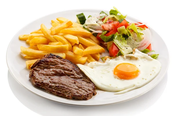 Grilled steaks, French fries, fried egg and vegetables — Stock Photo, Image