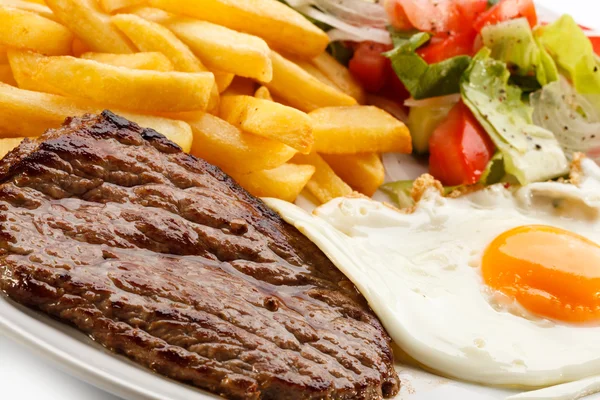 Grilled steaks, French fries, fried egg and vegetables — Stock Photo, Image