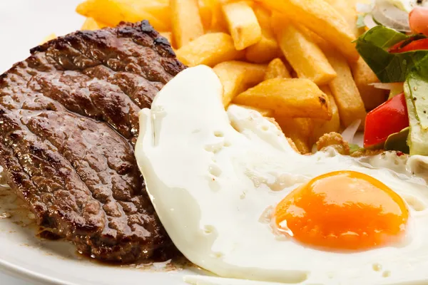 Bifes grelhados, batatas fritas, ovo frito e legumes — Fotografia de Stock