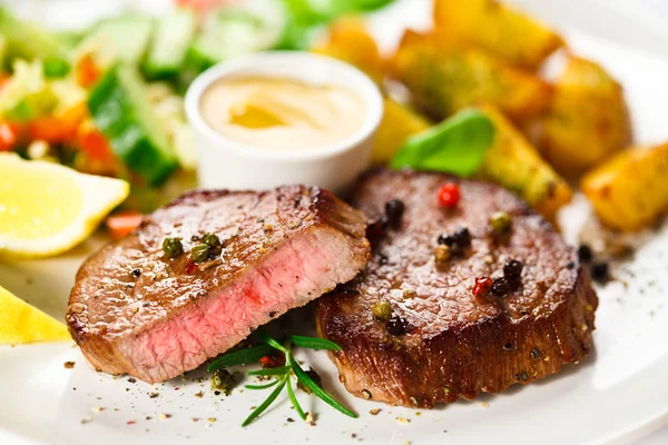 Gegrilde steaks, gebakken aardappelen en groentesalade — Stockfoto