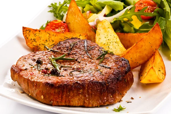 Gegrilde steaks, gebakken aardappelen en groentesalade — Stockfoto