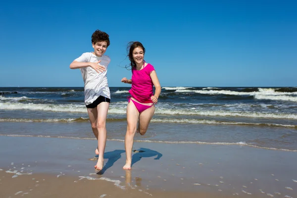 Teenage girl and boy jumping, running on beach — Stock Photo, Image