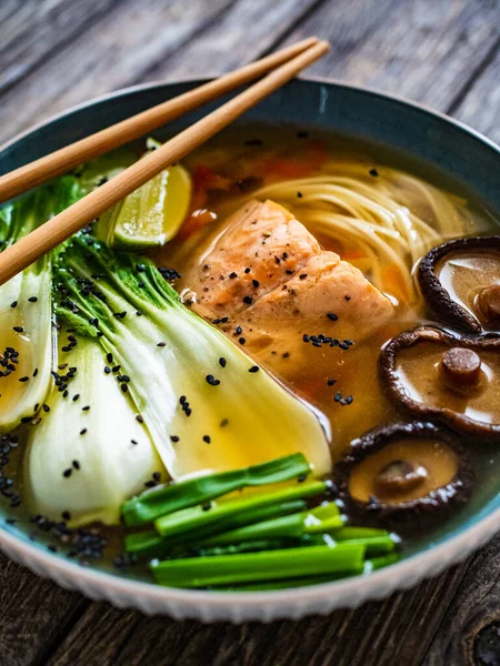 Asian style soup with fish, moon mushrooms, pak choi and noodles on wooden table