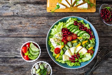 Tasty salad - leafy greens, camembert, pear, pomegranate, cherry tomatoes and broad bean on wooden table  clipart