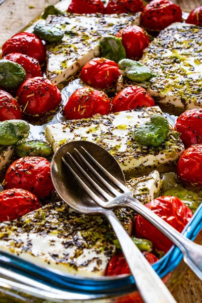 Roasted tomatoes with feta cheese and broad bean served in glass pan on wooden table