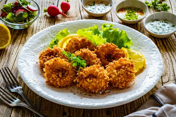 Fried breaded calamari rings with lemon and lettuce on wooden table