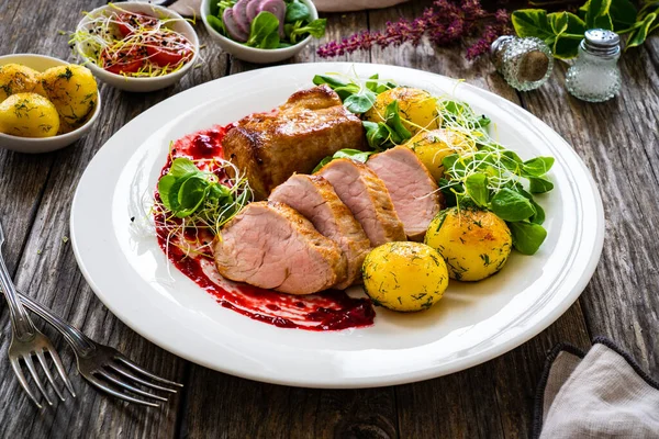 Fried pork loin with boiled potatoes and fresh vegetables on wooden table