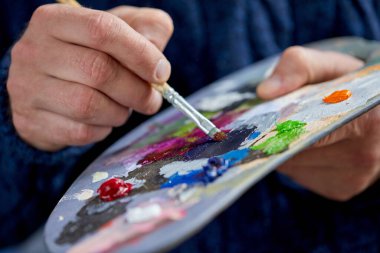 Closeup view of artist painting with palette, brush and acrylic colour paints in art studio indoors