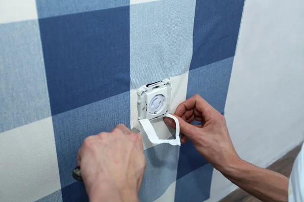 Decorador con bisturí colgando fondo de pantalla sobre el enchufe de la pared —  Fotos de Stock