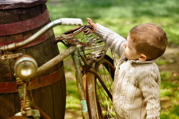 2 jaar oude nieuwsgierig babyjongen wandelen rond de oude fiets — Stockfoto