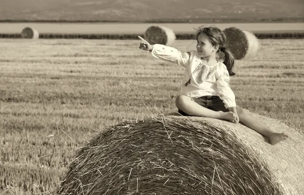 Small rural girl on the straw after harvest field with straw bal — Stock Photo, Image