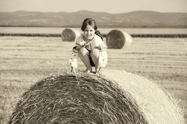 Pequena menina rural na palha após o campo de colheita com palha bal — Fotografia de Stock