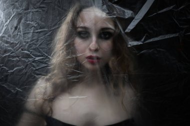 Genç, güzel, üzgün kadın COVID-19 'a karşı korunmak için plastik bir çarşafın arkasında mahsur kaldı. Tam kitap kapağına göre. 