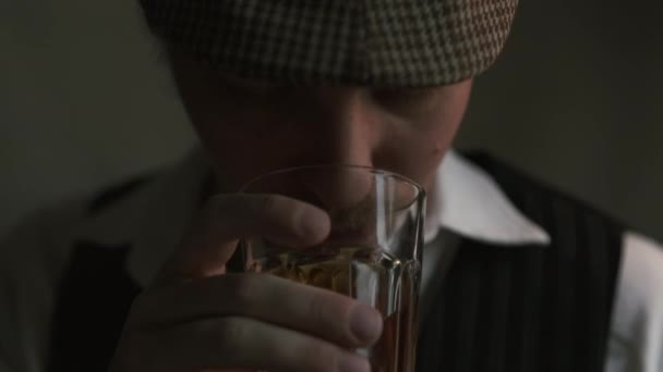 若い男がウイスキーを飲む レトロなスタイルで身に着けています ベレー帽で 映画撮影 大きなクローズアップ — ストック動画