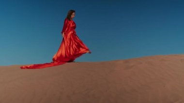 Kum tepelerinde dans eden kırmızı elbiseli Asyalı bir kadın.