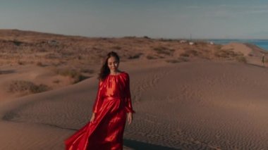 Kum tepelerinde dans eden kırmızı elbiseli Asyalı bir kadın.
