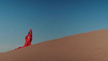 Kum tepelerinde dans eden kırmızı elbiseli Asyalı bir kadın.