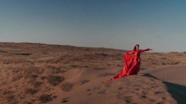 Kum tepelerinde dans eden kırmızı elbiseli Asyalı bir kadın.