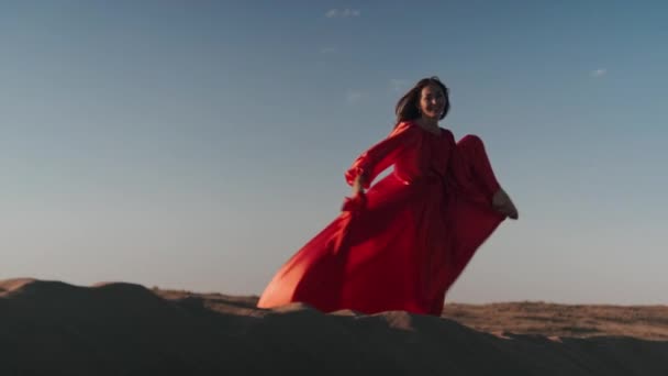 Kırmızı elbiseli Asyalı bir kadın kum tepelerinde tek ayak üstünde poz verir. — Stok video
