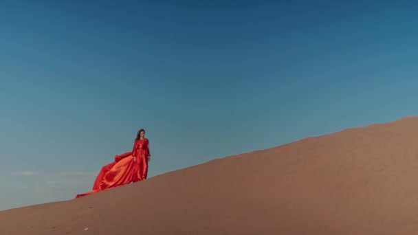 Kum tepelerinde dans eden kırmızı elbiseli Asyalı bir kadın. — Stok video