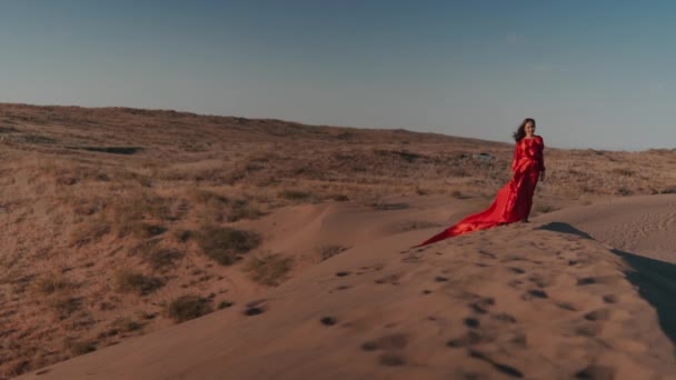 Una mujer asiática en un vestido rojo bailando en dunas de arena — Vídeos de Stock