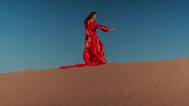 Una mujer asiática en un vestido rojo bailando en dunas de arena — Vídeos de Stock